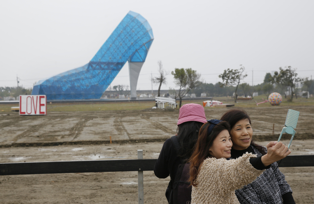 In this Jan. 28, 2016 photo, visitors take a selfie in front of a giant glass structure shaped like a high-heel shoe being built as a wedding hall in southern Chiayi, Taiwan. Completed recently, the transparent 17-meter (55-foot) tall structure in Chiayi countys Southwest Coast National Scenic Area has already begun attracting large numbers of visitors even before its official opening in two weeks. (AP Photo/Wally Santana)